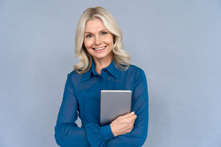 Happy middle aged business woman holding digital tablet isolated on grey wall.