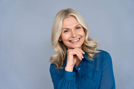 Happy sophisticated middle aged business woman looks at camera isolated on grey.