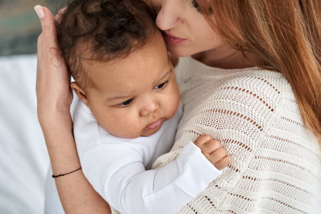 Loving caucasian mother hugging cute infant african american baby daughter.の写真素材