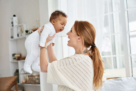 Happy caucasian mother having fun lifting cute little baby daughter.の写真素材