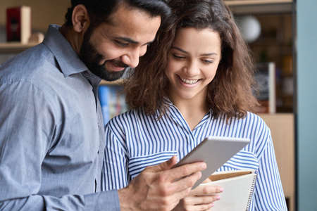 Smiling indian and latin colleagues talking using digital tablet in office.の写真素材