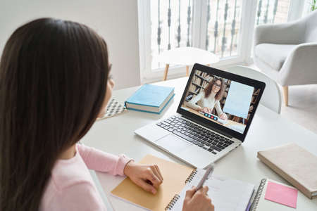 Indian kid girl having virtual class with online teacher learning at home.