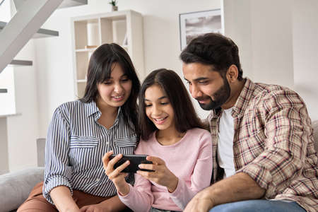 Happy indian family and teen daughter using smart phone at home.