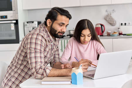Young indian father helping school child teen daughter studying online at home.の写真素材