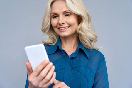 Shot of senior 50s aged blonde female manager using phone isolated on gray
