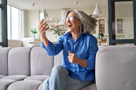 Surprised exited mature woman 60s aged at home with cellphone.の写真素材