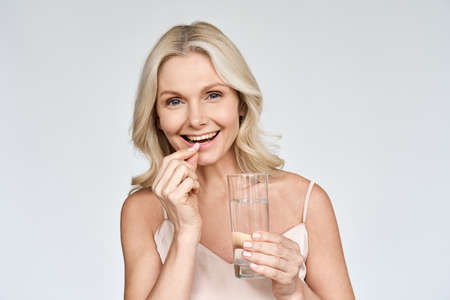 Portrait of happy smiling mid aged woman taking pills isolated on white.の写真素材