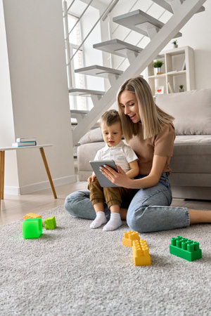 Smiling mum teaching toddler child son using digital tablet at home.