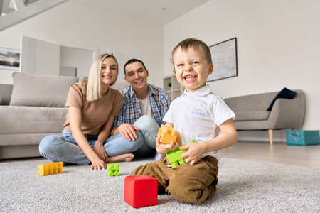 Cute happy kid toddler son playing toys with young parents at home.