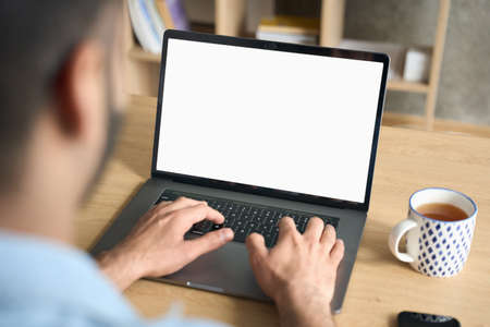 Indian businessman typing working using laptop at home office. Mockup screen.