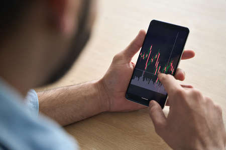Closeup brokers hands holding cellphone with stockmarket and graphs.