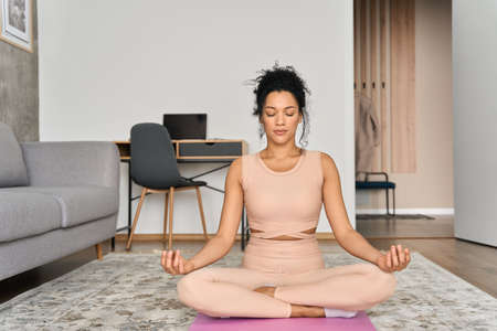 Young attractive African American girl sitting at home in deep meditation.の写真素材