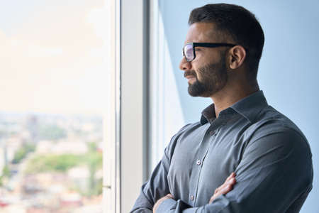 Headshot portrait of businessman standing in office looking away in window.