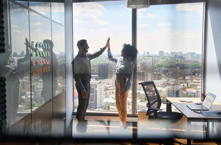 Multiracial business partners giving high five celebrating victory in office.