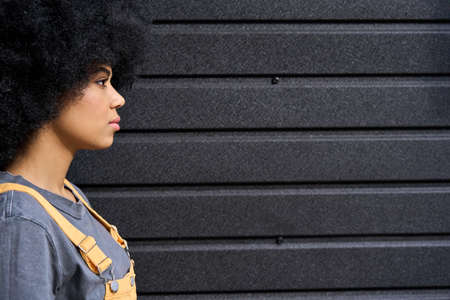 Young pretty afro girl profile with curly hair standing on black wall background.の写真素材