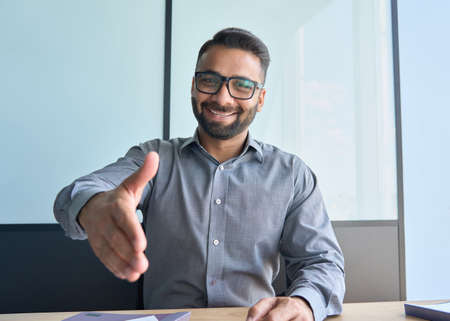 Confident smiling indian boss giving hand greeting partner in corporate office.の写真素材