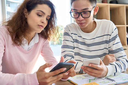 Multicultural coworkers using cellphones together at desk in modern office.