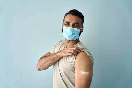 Happy Indian man wearing face mask showing bandage after getting vaccination.の写真素材