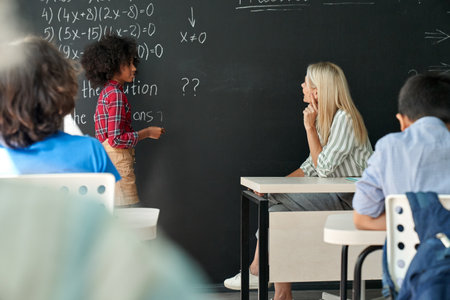 Afro American schoolkid answering task to teacher near chalkboard in classroom.の写真素材