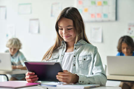 Happy smiling schoolgirl reading task from tablet computer device in classroom.の写真素材