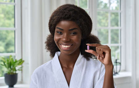 Young pretty happy smiling black girl holding beauty pill. Headshot portrait.の写真素材
