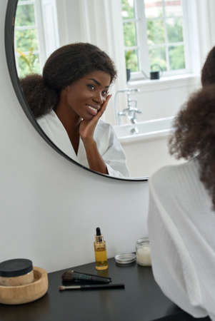 Young black beauty girl touching face looking at mirror in bathroom at home.の写真素材