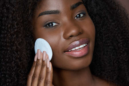 Black young woman holding cotton pad removing face make up with makeup remover.の写真素材