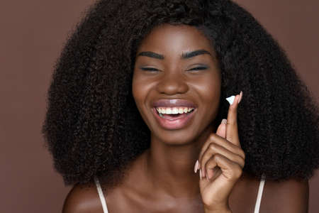 Happy young black woman applying facial cream isolated on brown background.の写真素材
