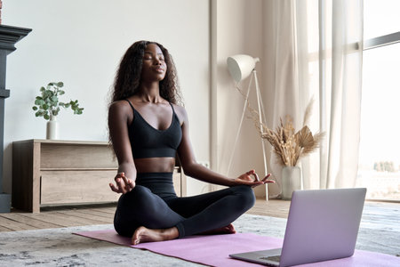 Young calm fit healthy African black woman at home doing yoga learning online class.の写真素材