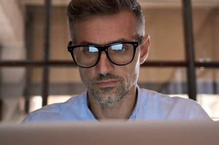 Concentrated business man looking at computer screen reflecting in glasses.の写真素材