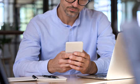 Closeup of businessman male hands holding using smartphone in office.の写真素材