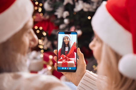Happy senior grandparents greeting grandchild open Christmas gift on video call.