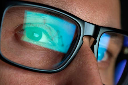 Trader looking at computer screen analyzing trading chart reflecting in glasses.の写真素材