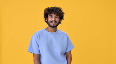 Smiling young indian guy standing isolated on yellow background.