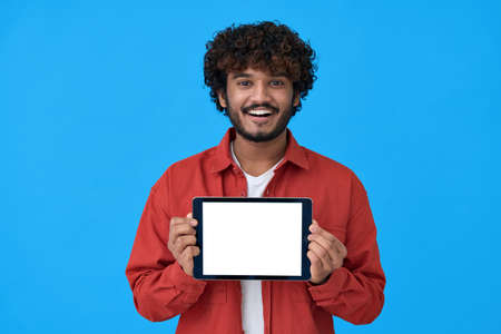 Happy young indian man showing big mockup tablet screen on blue background.