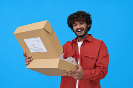 Happy indian young man holding open parcel box isolated on blue background.の写真素材