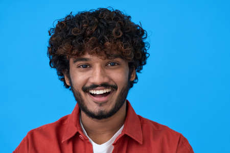 Happy young indian guy laughing isolated on blue background. Headshot portraitの写真素材
