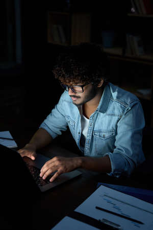 Young indian business man student working online at night using laptop.の写真素材