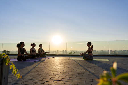 Multiethnic young women meditate with yoga teacher during group class outdoor.の写真素材