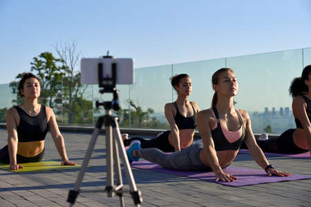 Women group streaming online yoga class recording tutorial outdoor on phone.の写真素材