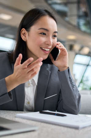 Happy young chinese business woman talking on phone working in office.の写真素材