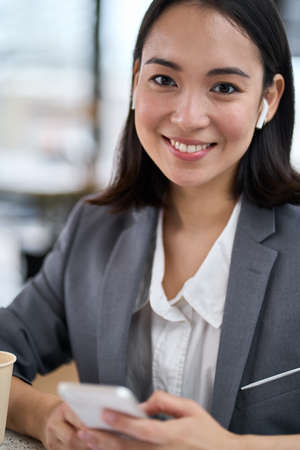 Young smiling Asian business woman wearing suit using phone. Portrait