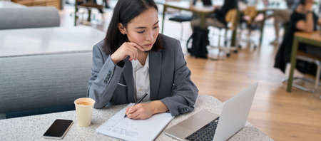 Young serious Asian business woman using laptop working in modern office.