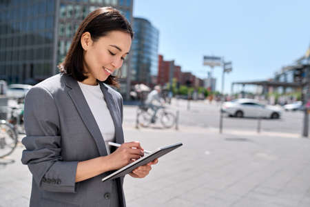 Young happy Asian business woman executive using digital tablet on city street.の写真素材