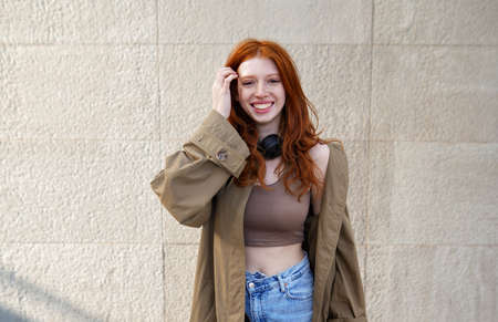 Happy teen redhead girl looking at camera standing on urban wall background.の写真素材