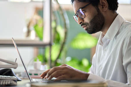 Busy indian business man programmer working typing on laptop sitting at desk.