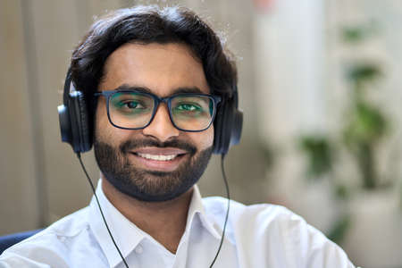 Smiling indian business man wears headphones looks at camera, headshot portrait.の写真素材