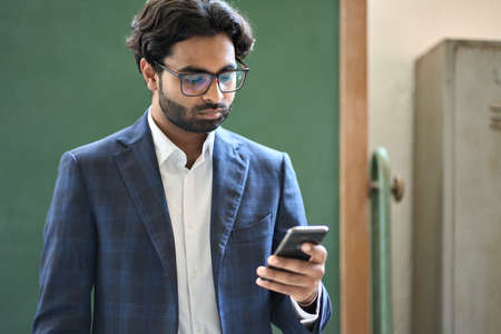Young indian business man using smartphone working standing in office.の写真素材
