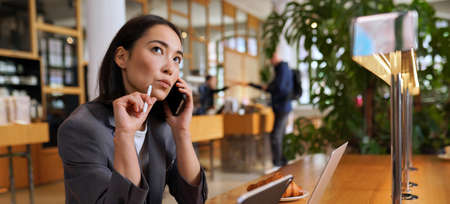 Doubtful Asian business woman talking on phone making call and thinking.