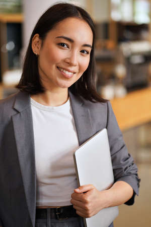 Smiling young Asian professional woman wearing suit, vertical portrait.